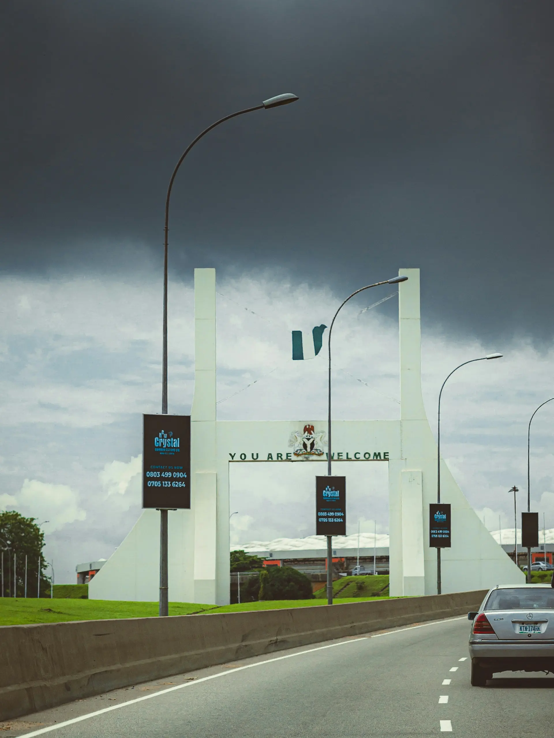 Abuja City Gate on the expressway under a stormy sky, Nigerian flag flying