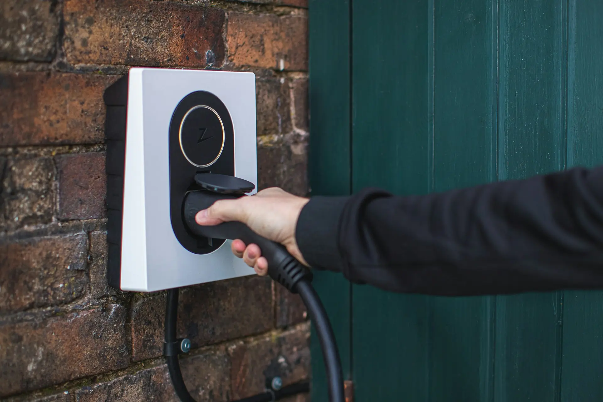 A hand plugging a charging cable into a wall-mounted home EV charger